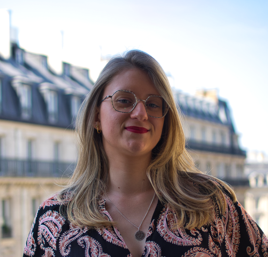 Femme avec des lunettes devant un immeuble, portant un haut cachemire et un collier.