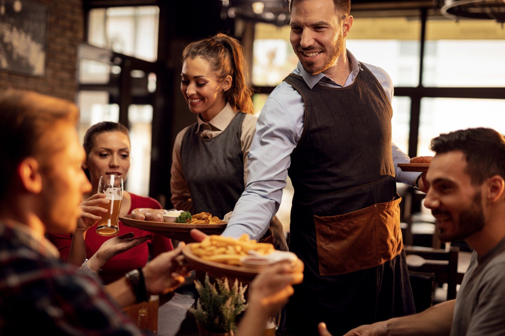 Happy waiters bringing food at the table and serving group of friends in a restaurant.