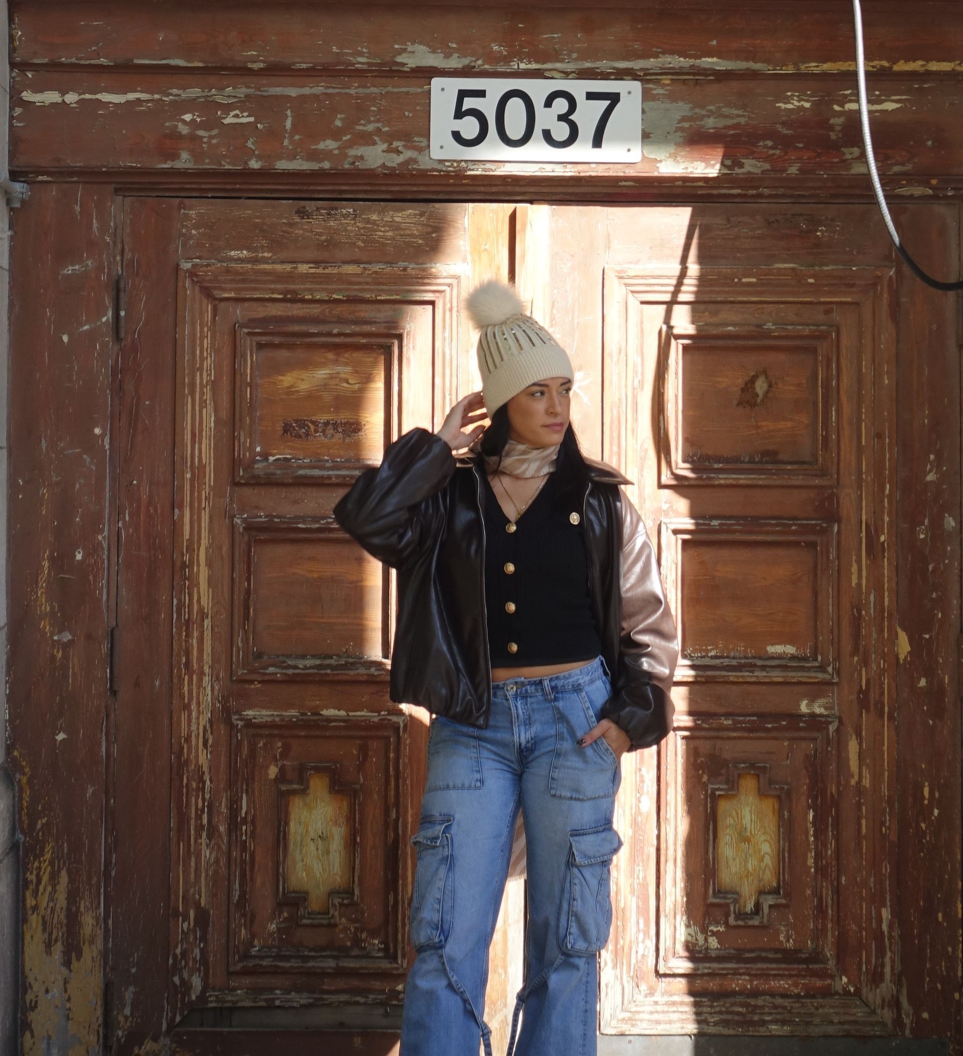 Woman in a knit cap and jacket stands in front of a weathered wooden door marked 5037.