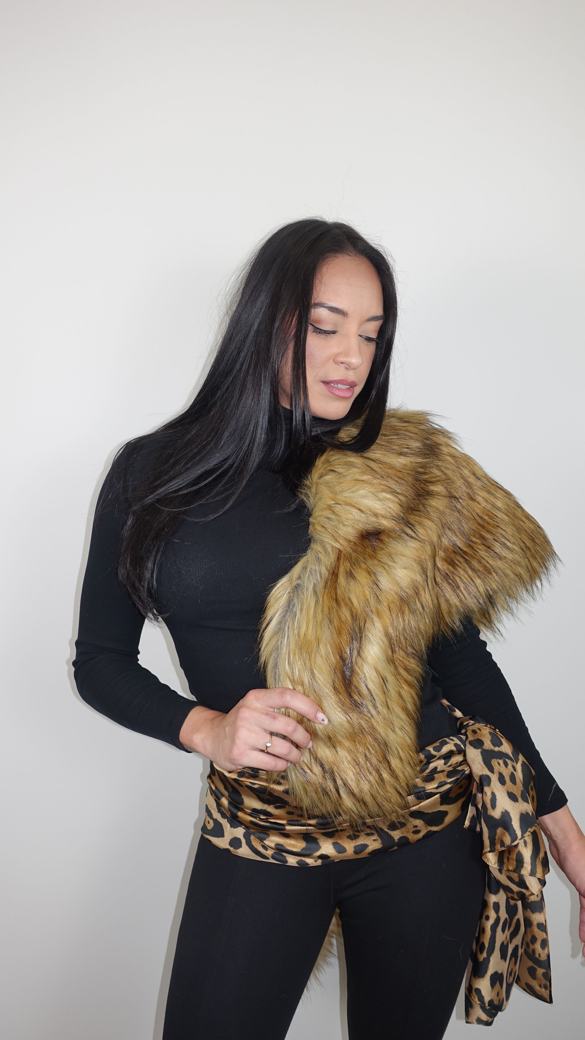 Woman wearing a black top, scarf with faux fur and leopard print, and black pants.