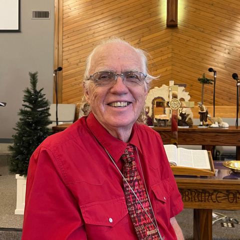 Smiling man in red shirt and tie at church altar.