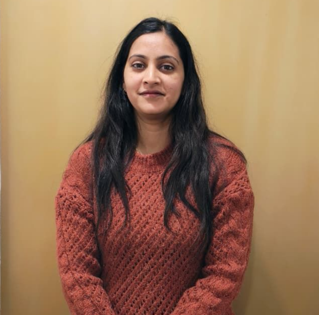 A man is sitting at a table holding a cup of coffee and using a laptop computer.