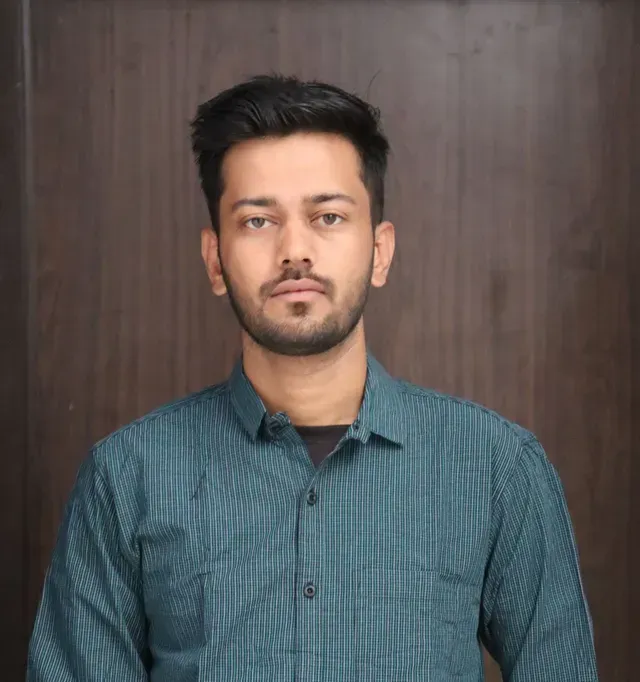 A man is sitting at a table holding a cup of coffee and using a laptop computer.