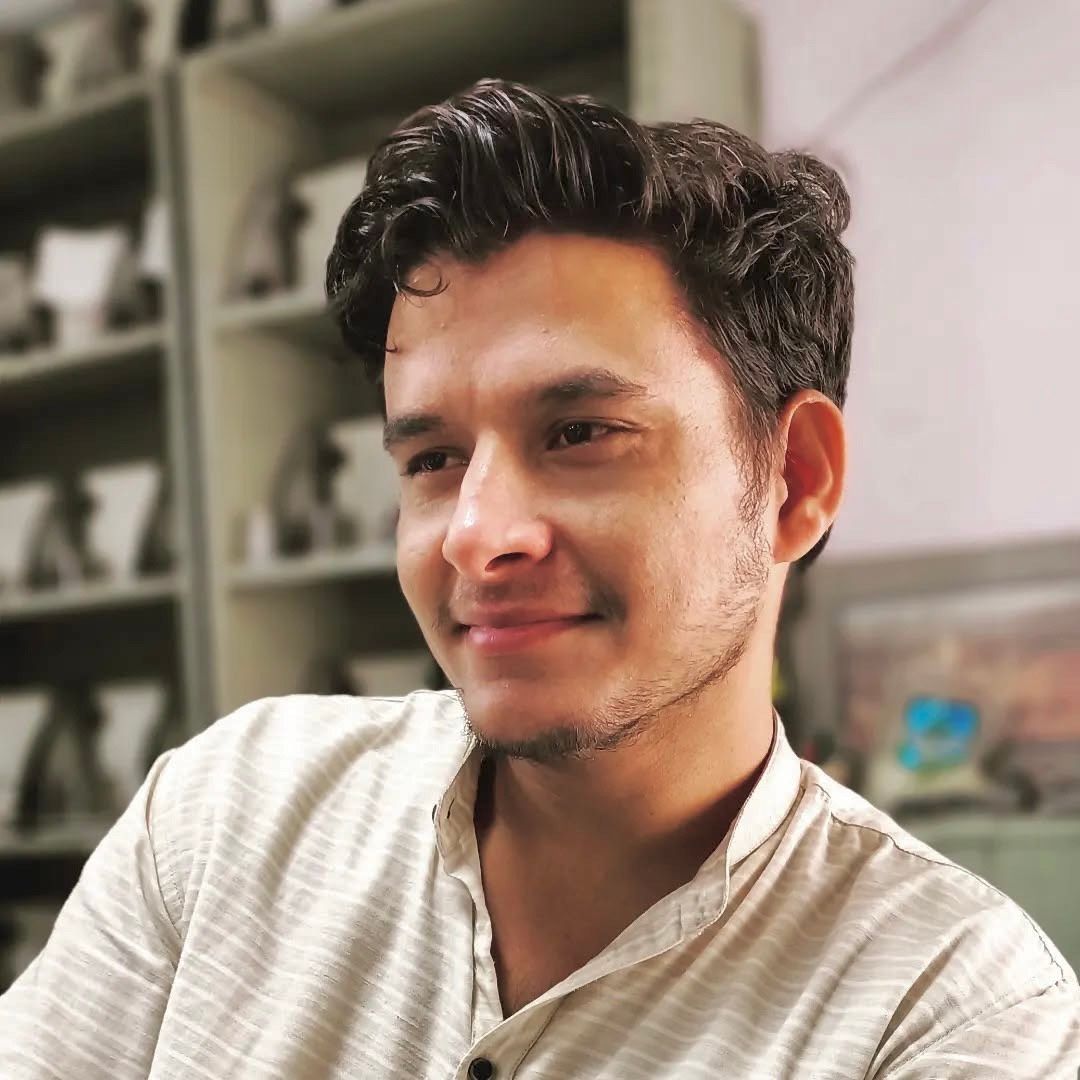A man is sitting at a table holding a cup of coffee and using a laptop computer.