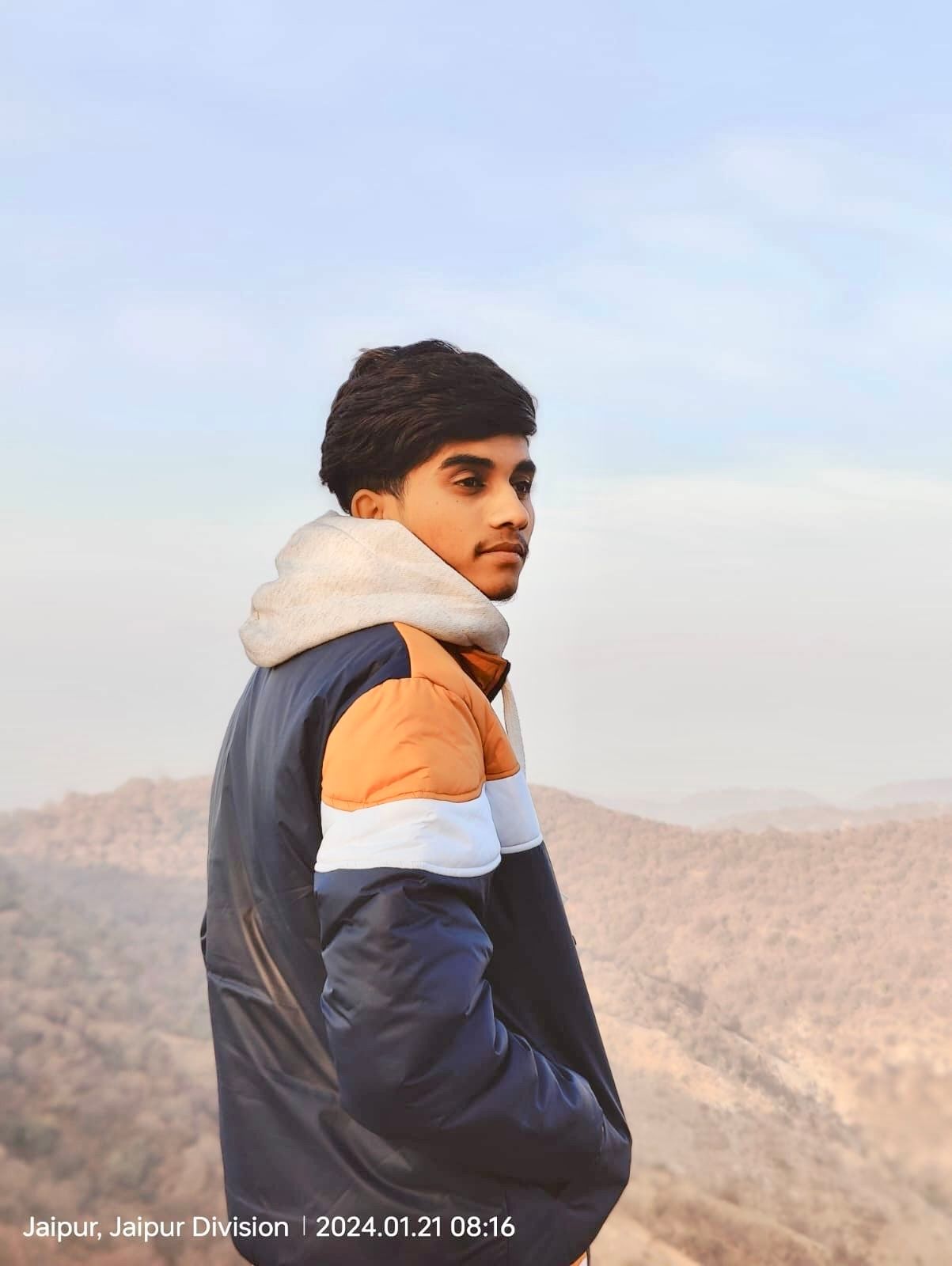 A man is sitting at a table holding a cup of coffee and using a laptop computer.