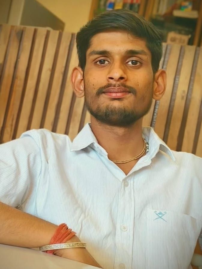 A man is sitting at a table holding a cup of coffee and using a laptop computer.
