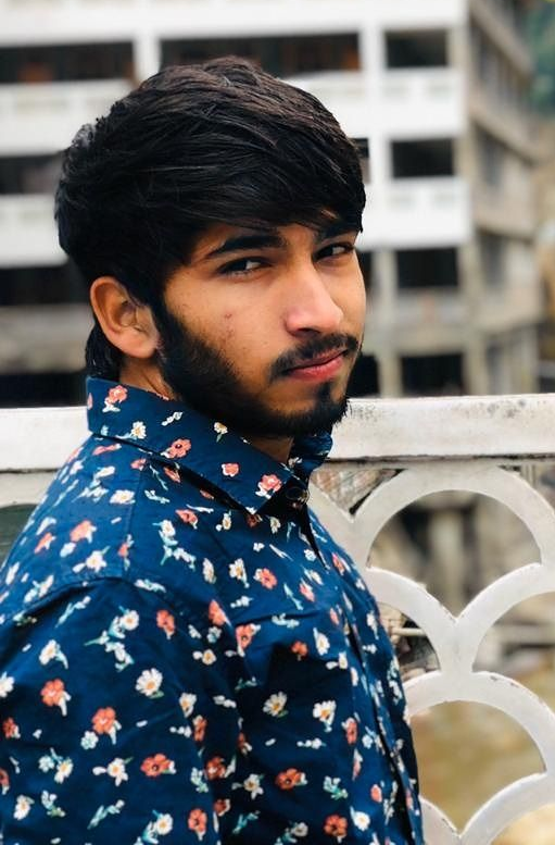 A man is sitting at a table holding a cup of coffee and using a laptop computer.