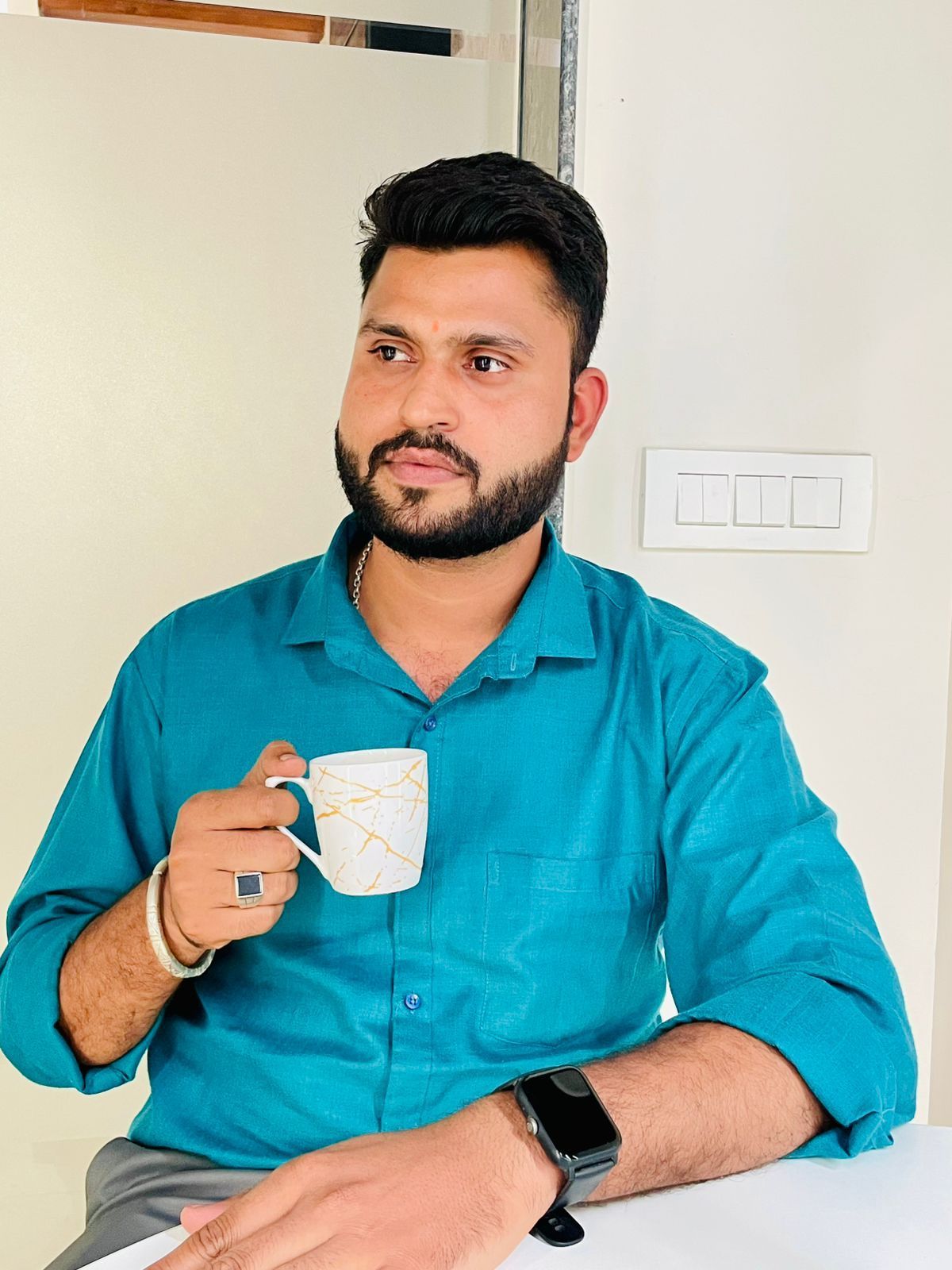 A man is sitting at a table holding a cup of coffee and using a laptop computer.