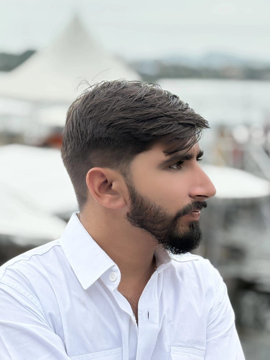A man is sitting at a table holding a cup of coffee and using a laptop computer.