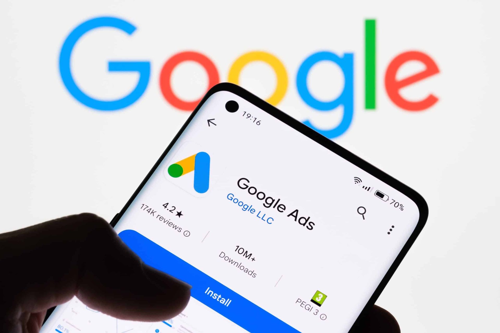 Hand holding smartphone displaying Google Ads app, with Google logo in background.