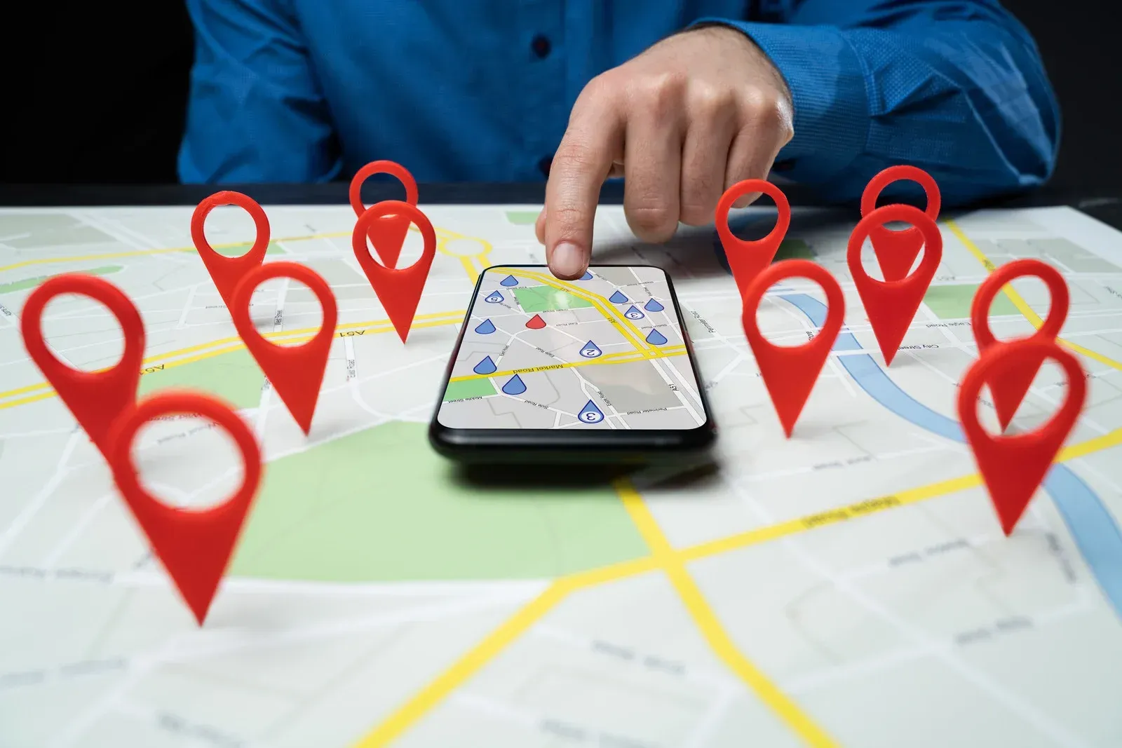 Person using a phone on a map with red location markers, choosing a location.