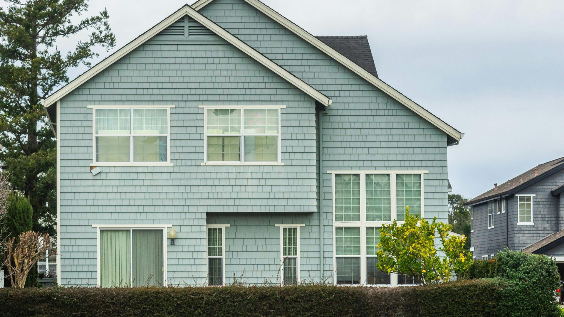 A two-story suburban home with gray siding, blue accents, a two-car garage, and landscaping under a cloudy sky.