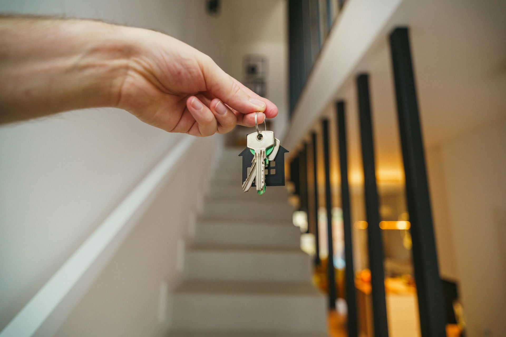 Hand holding a small keychain in front of a stairway and windowed hallway