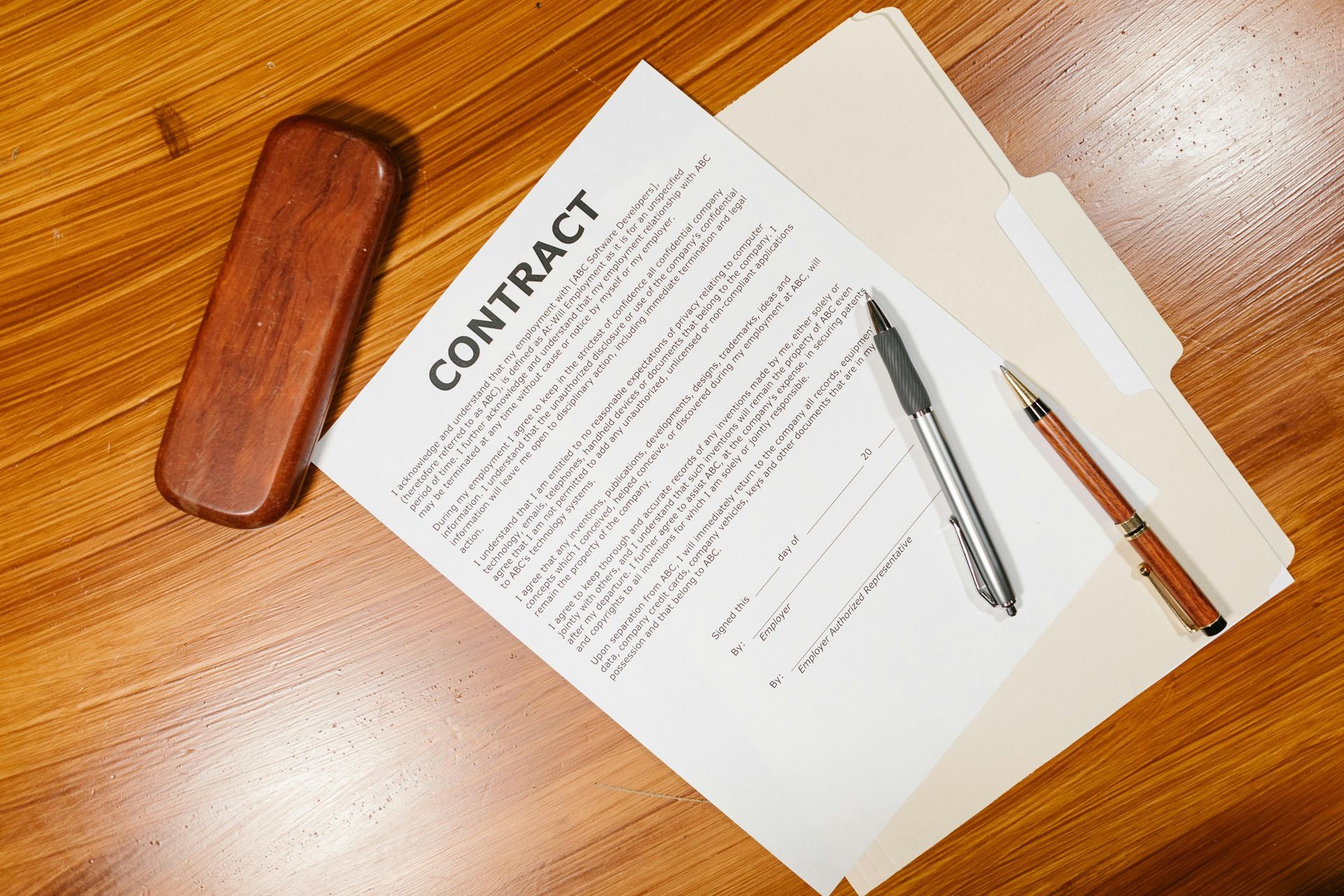 Contract document on a wooden desk with glasses case, pen, and pencil alongside pages.