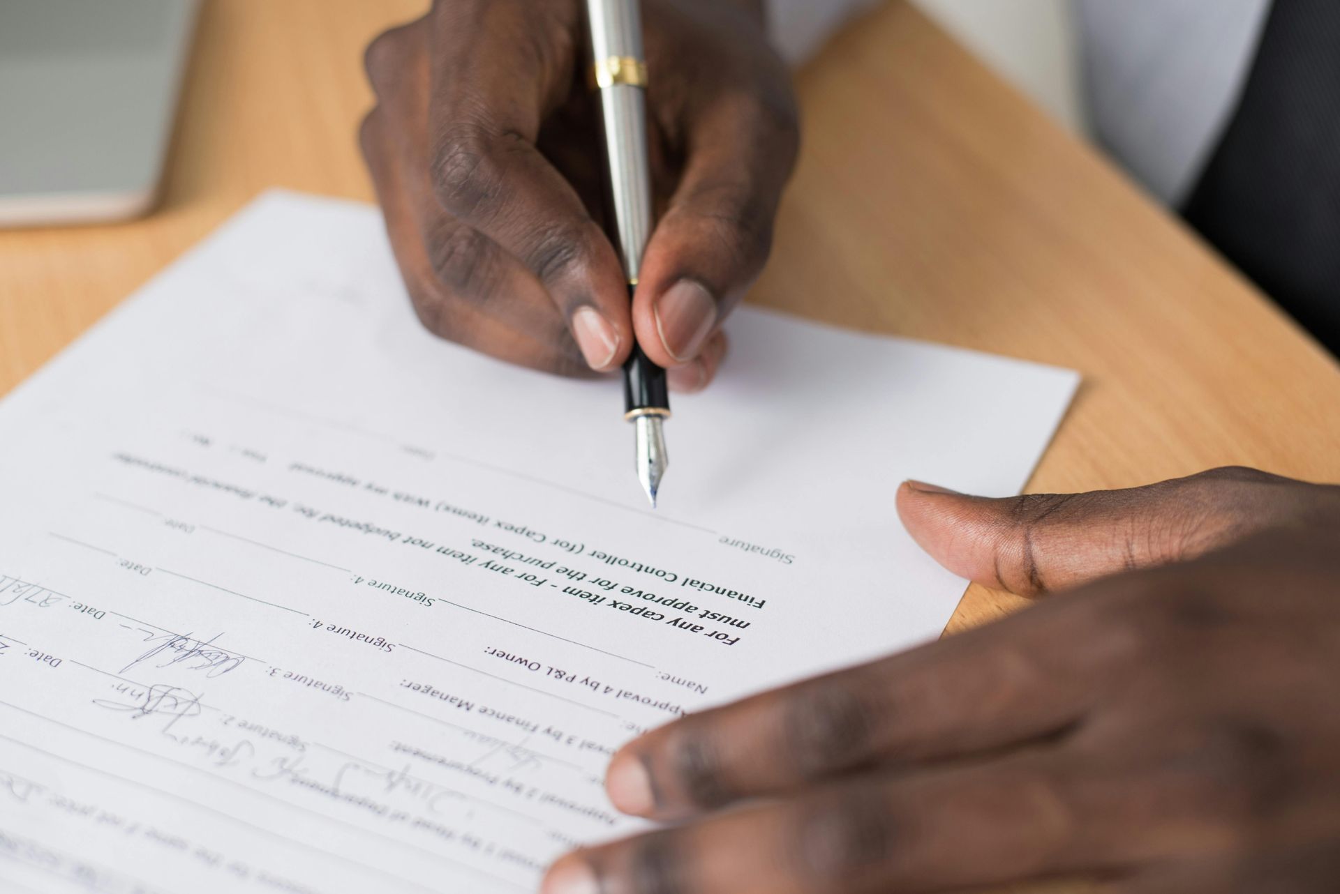 Close-up of hands using a fountain pen to sign a document on a wooden desk.