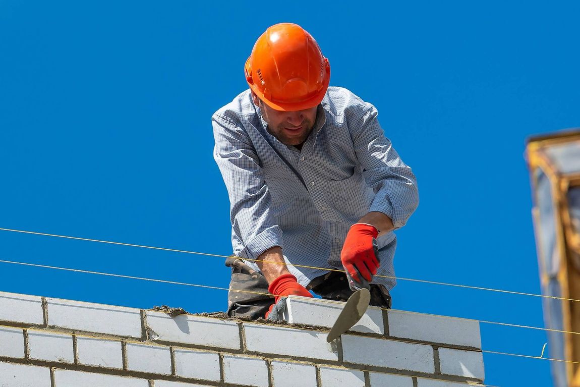 a man wearing a hard hat and gloves is working on a brick wall
