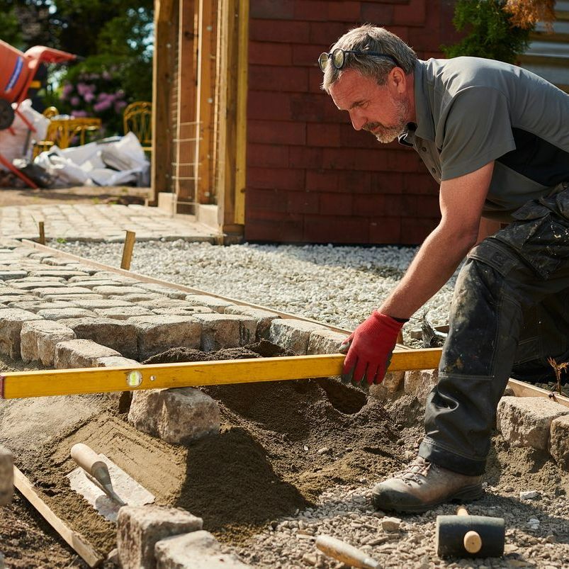 A man wearing red gloves is working on a brick walkway