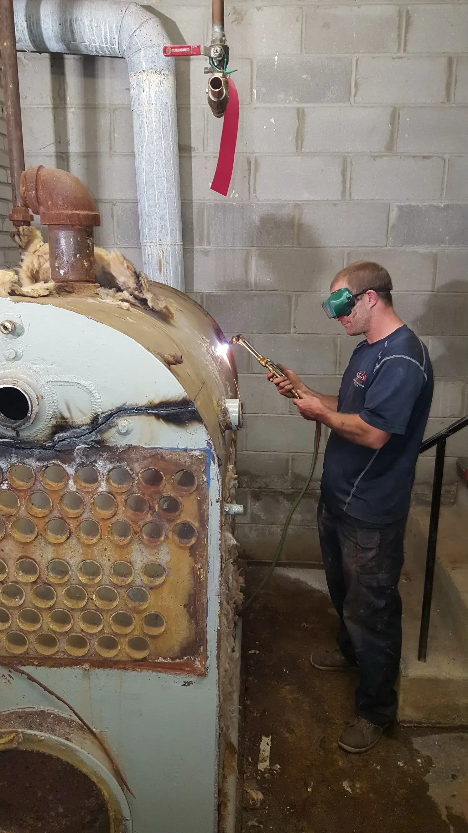A man is welding a piece of metal in a basement.