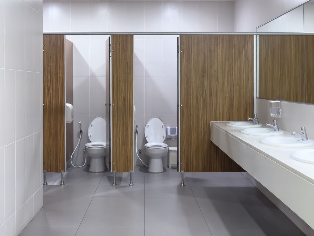 Modern restroom with stalls, white sinks, mirrors, and wood-paneled partitions