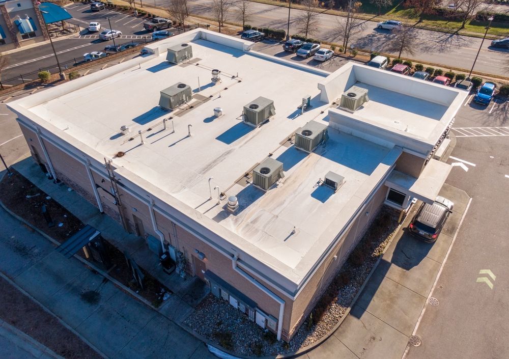 Aerial view of a flat-roofed commercial building with rooftop HVAC units and surrounding parking lot.