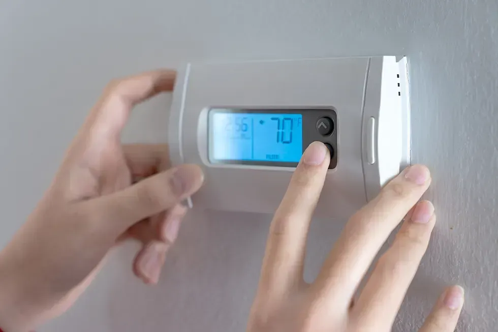 A woman is pressing the down button of a wall attached house thermostat