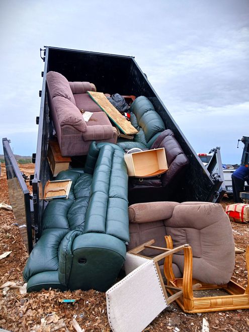 Furniture piled in a crushed truck trailer after a crash, with sofas and chairs scattered around.
