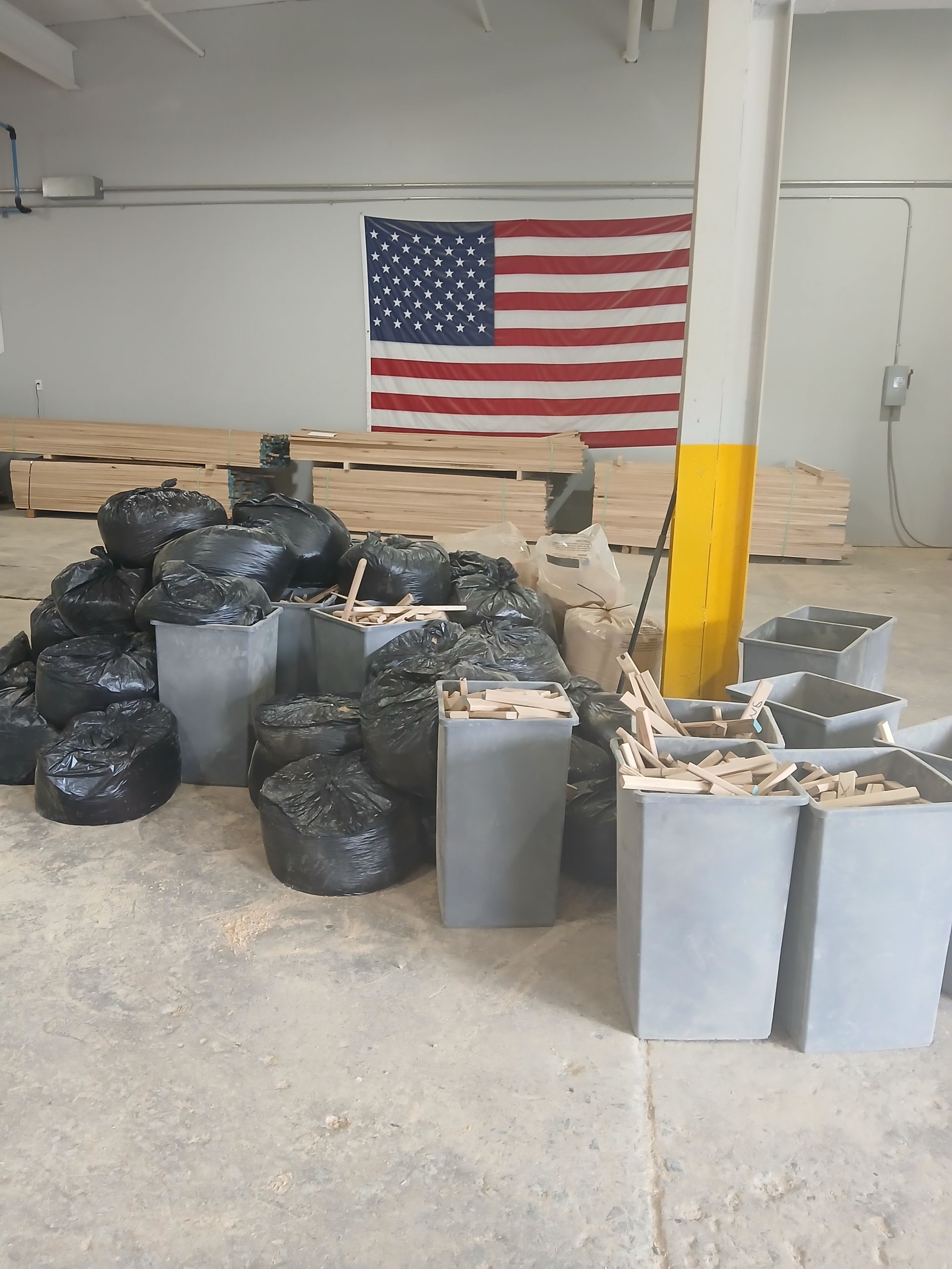 Black trash bags and gray bins in a warehouse, with a large American flag on the wall.