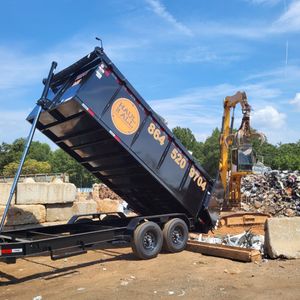 Black dump trailer tipped steeply at a construction site beside excavators and piles of debris.