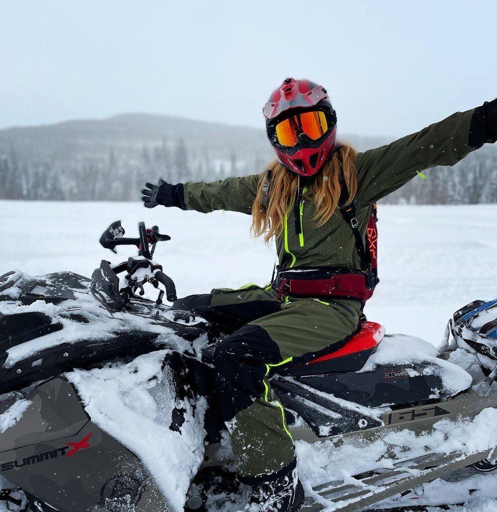 female snowmobile rider posing on polaris snowmobile in snowy mountains