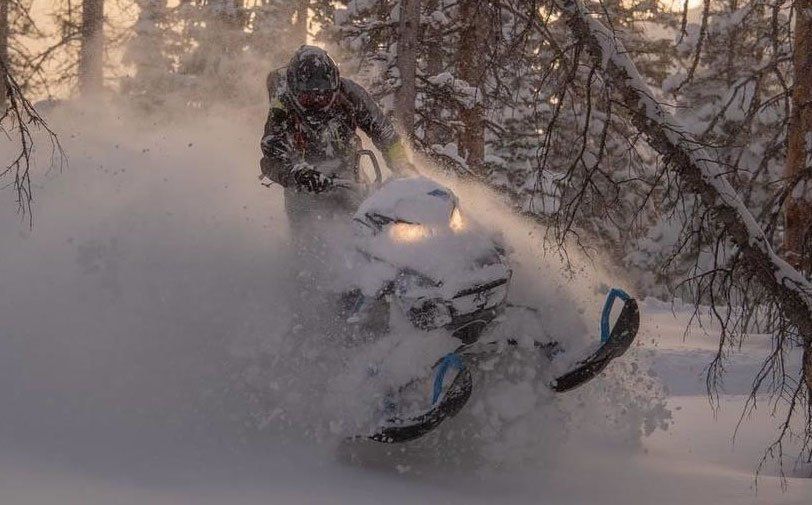Snowmobile rider riding a snowmobile through a forest