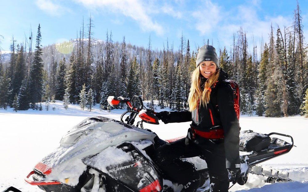 Tracked Out Adventure guide sitting on snowmobile in mountain scenery