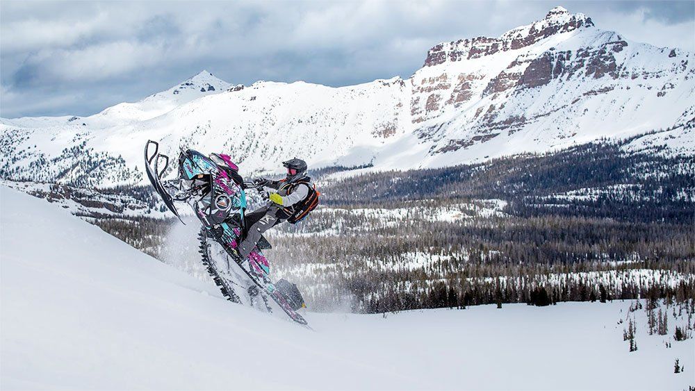 Snowmobile rider performing a jump trick in the mountains