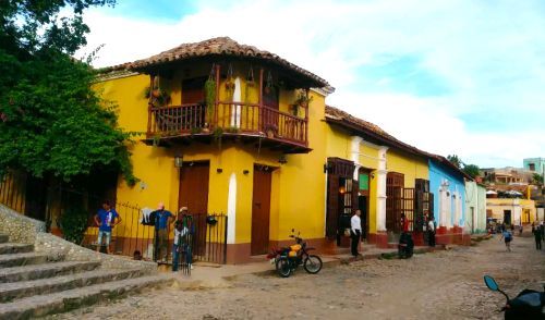 Yellow building with balcony on a cobblestone street in Trinidad, Cuba. People stand around.