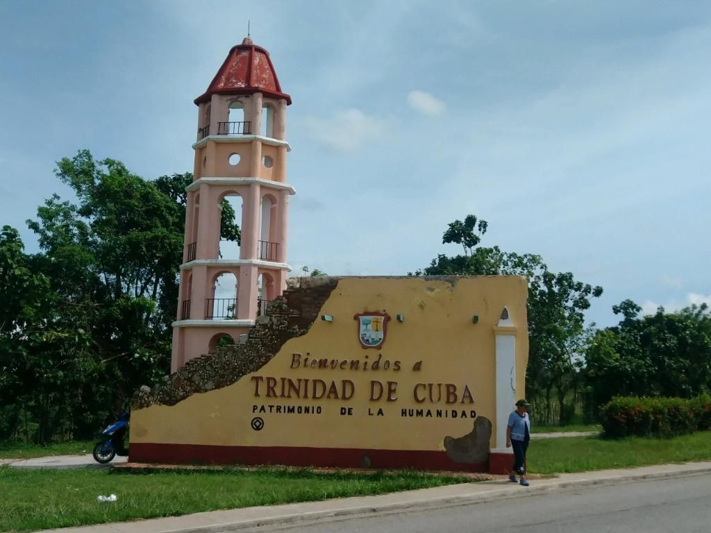 Sign welcoming visitors to Trinidad de Cuba, with a tower and person.