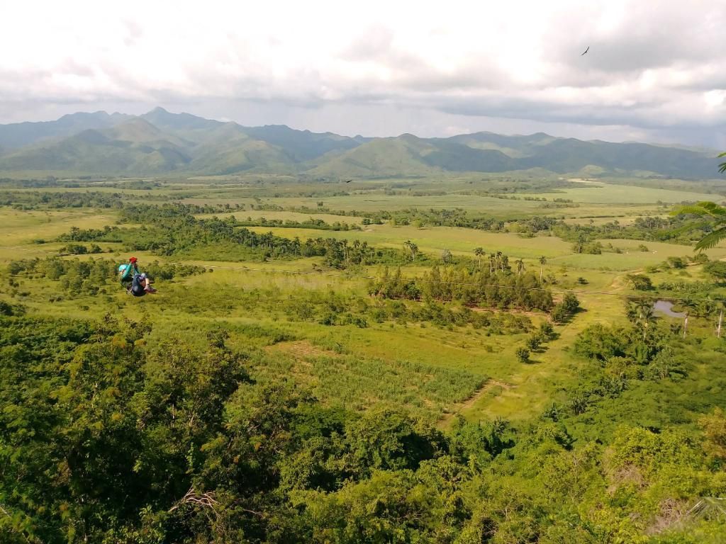 Overlooking a vast green valley with distant mountains and a person hiking.