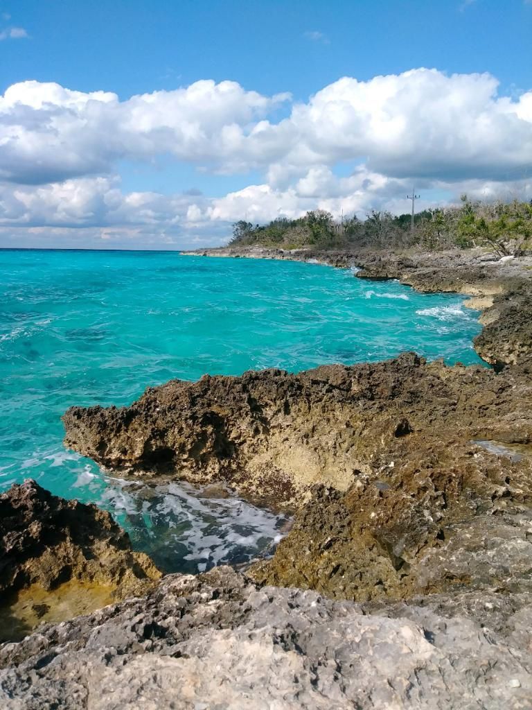 Turquoise ocean waves crashing against a rocky shoreline under a partly cloudy sky.