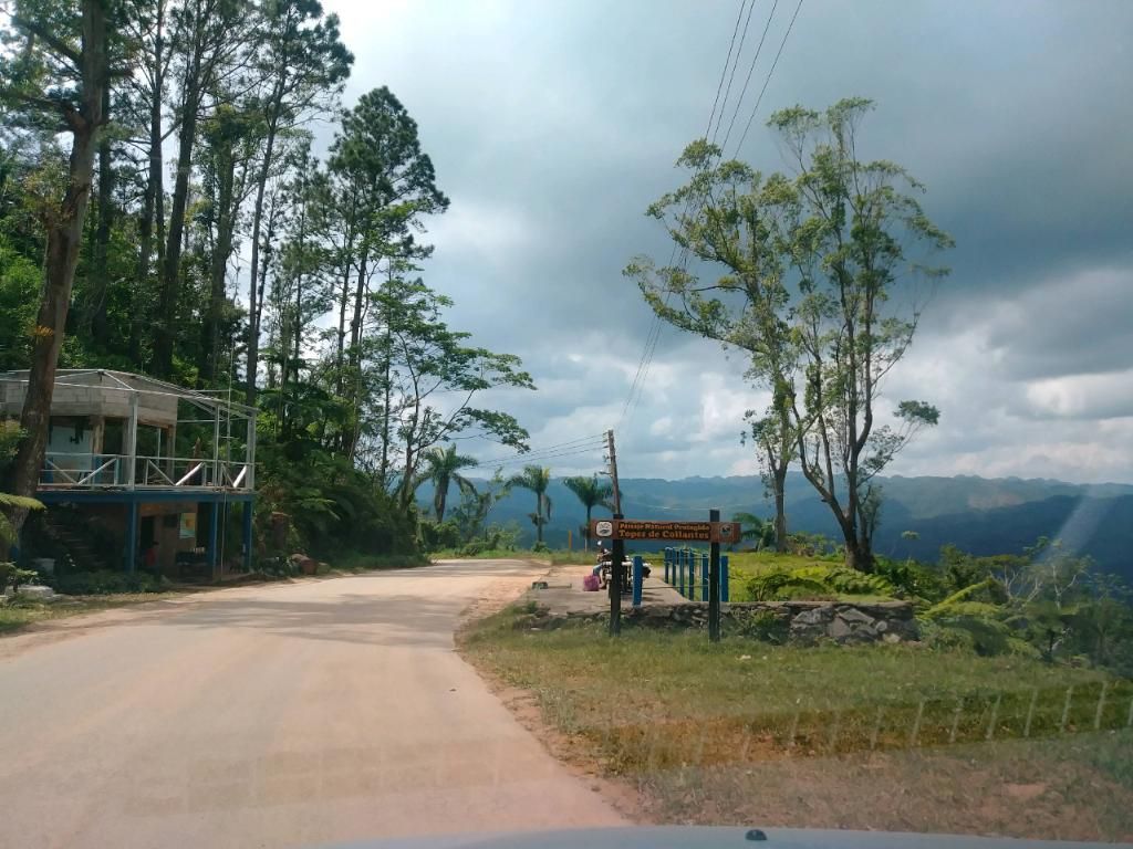 Dirt road leads to a lookout point with a sign and distant hills under a cloudy sky.