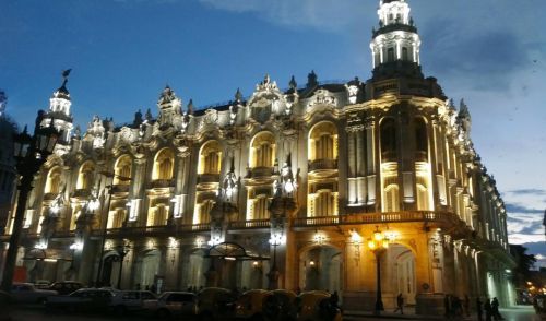 Lit-up ornate building at night, Havana, Cuba. Exterior with arched windows, multiple levels, and tower.