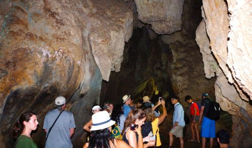 People exploring a cave with stalactites. Brown and yellow cave walls. Tourists are looking and taking photos.