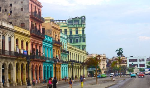 Colorful buildings line a Havana street, people walk, cars drive.