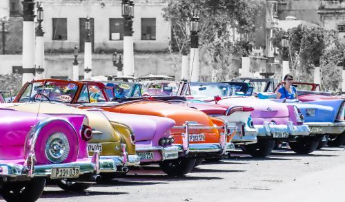 Classic colorful convertible cars parked in a row, with a building in the background.