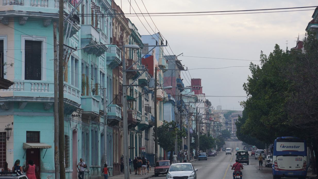 A street in Havana with colorful buildings, cars, trees, and power lines.