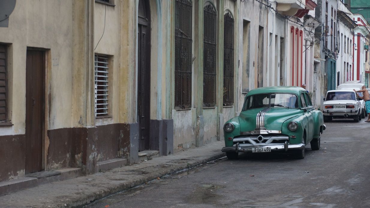 Green vintage car parked on a street in Havana, Cuba, next to a weathered building.