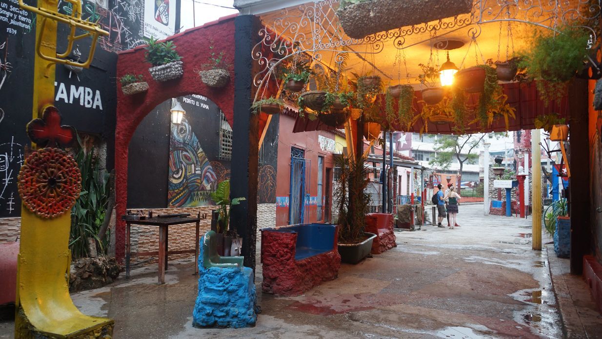 Colorful alleyway with archway, plants, and string lights overhead.