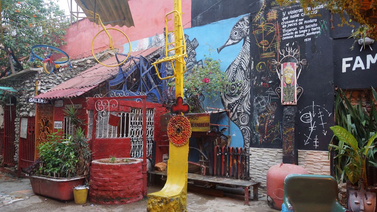 Colorful, artistic courtyard with painted walls, plants, and found-object sculptures.