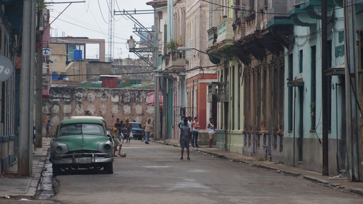 Street scene in Havana, Cuba, with colorful, old buildings and a classic green car parked on the side.