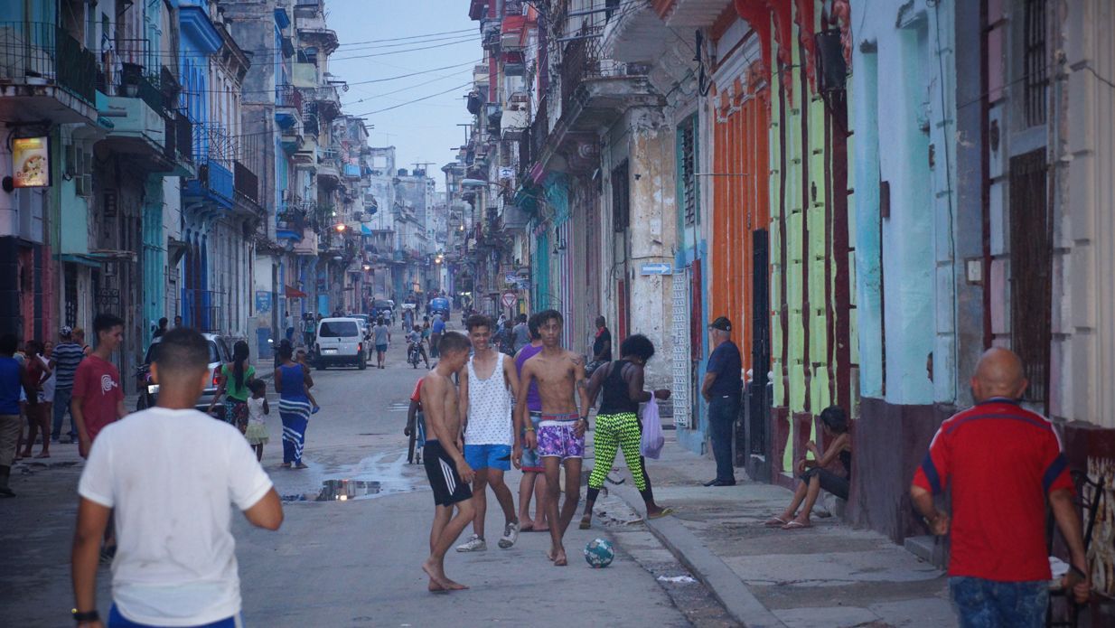 Street scene in Havana: people walking in street, colorful buildings line the road.