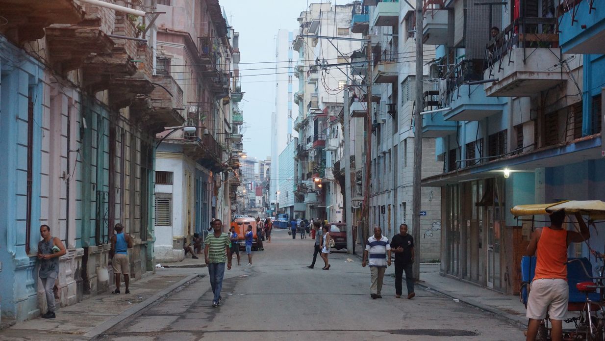 Street in Havana, Cuba, lined with buildings; people walking and standing on the road.