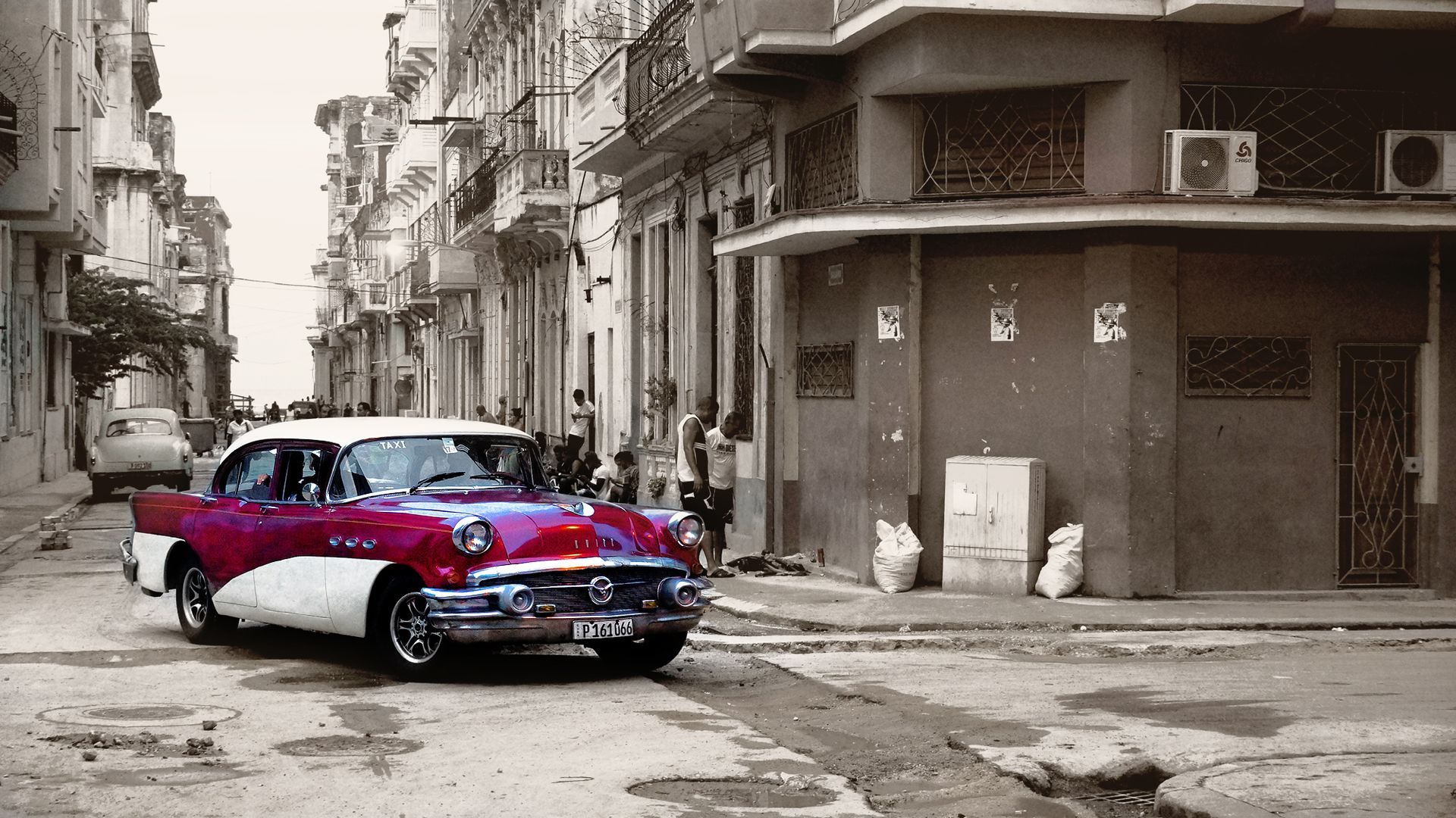 Classic red and white car driving down a Havana street with colonial buildings.