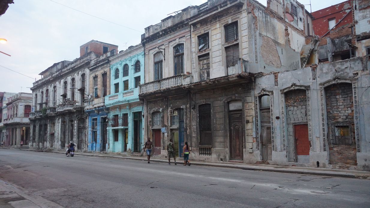 Row of weathered, colorful buildings in Havana, Cuba. People walk on the street in front.